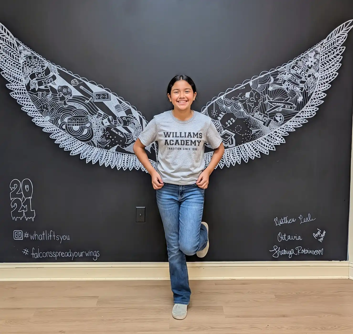 Williams Academy student posing in front of a wings mural